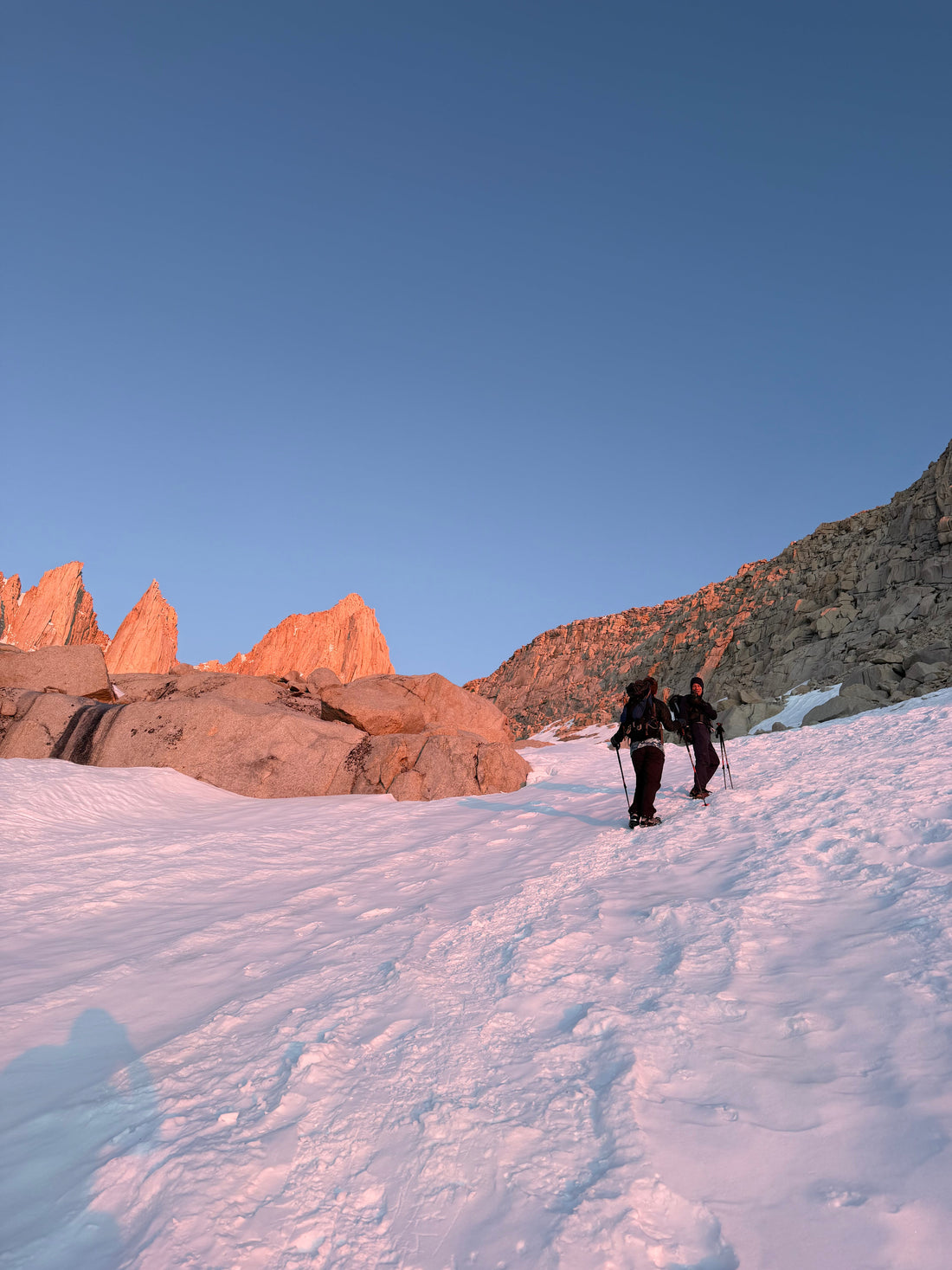 Two hikers with trekking poles climbing a snowy mountain at sunrise — mineral sunscreen for high-altitude UV protection on long hikes